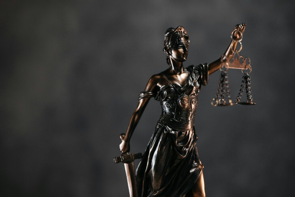Detailed bronze Lady Justice statue with scales and sword against a dark background, symbolizing law and justice.